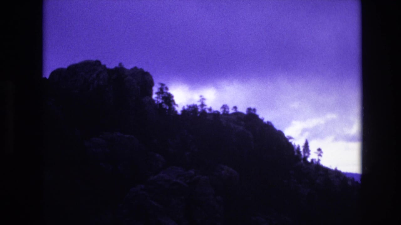 Dark ridge and evergreen trees against bright storm clouds.