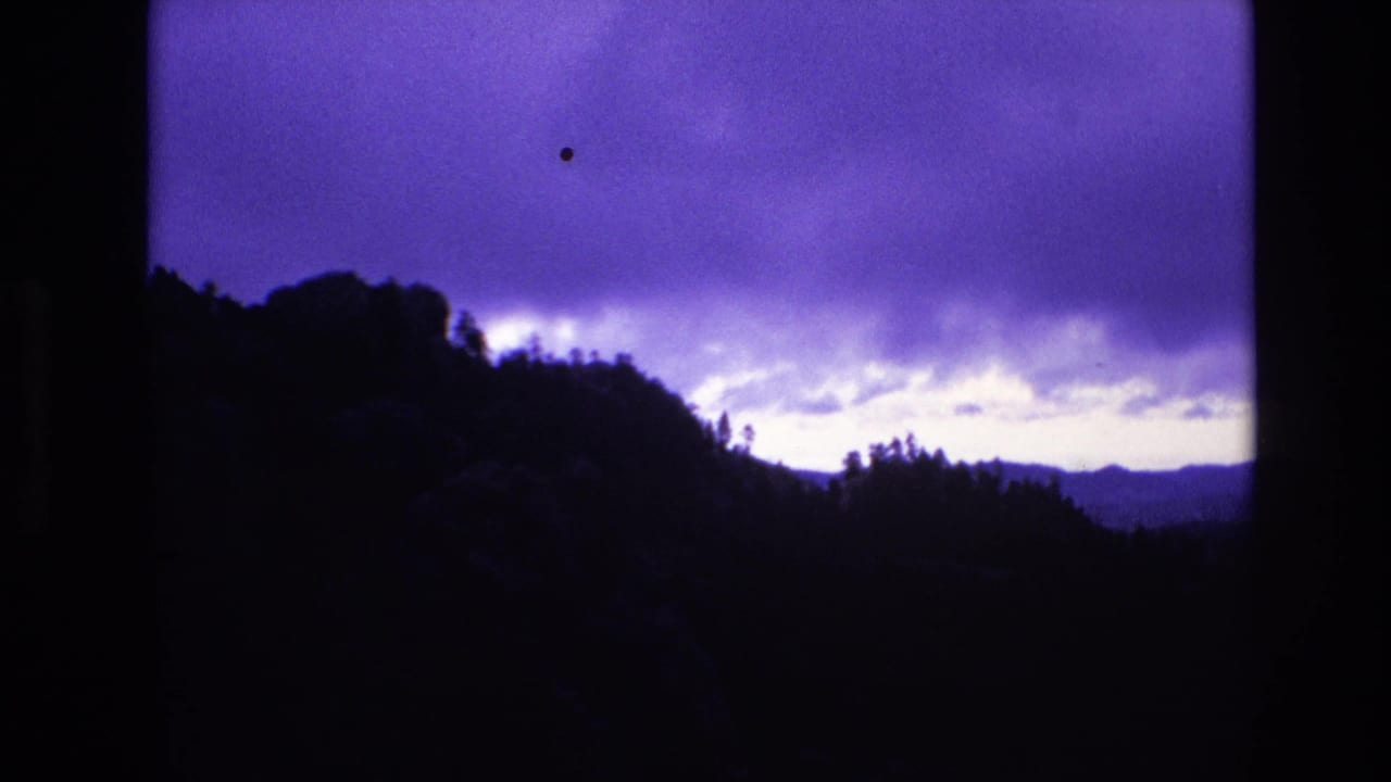 South Dakota 1974 8mm frame showing a dark wooded ridgeline beneath a purple twilight sky with layered clouds and low-light grain.
