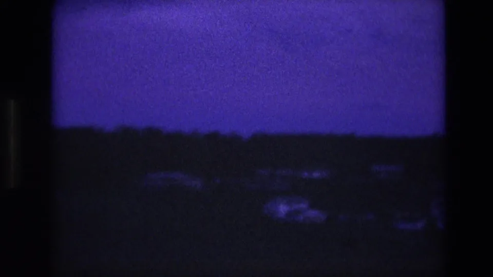 South Dakota 1974 8mm frame showing a dark rural landscape, faint pale shapes near the lower edge, and a purple evening sky.