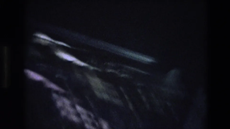 Low-exposure 8mm transitional frame showing blurred pale streaks against a nearly black field, likely from camera movement or underexposure.