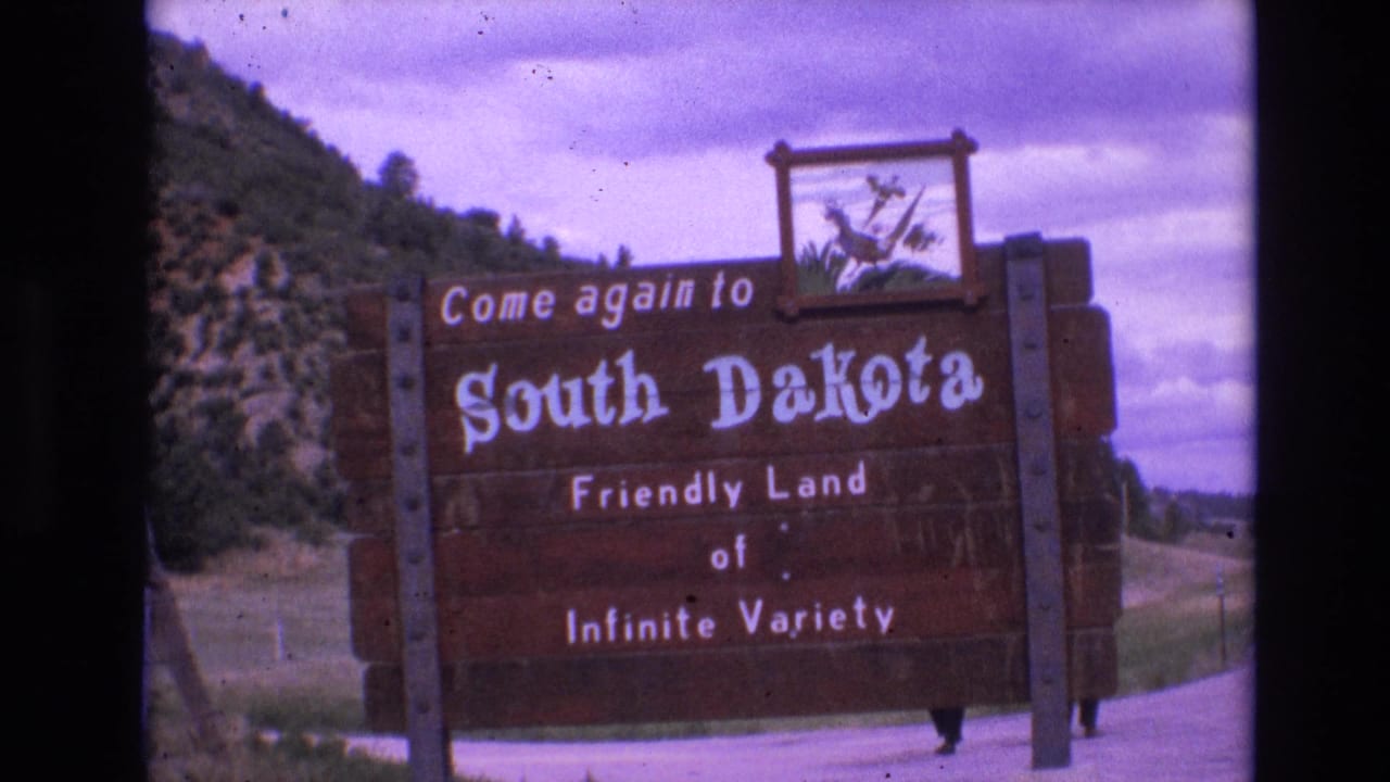South Dakota roadside sign with cloudy sky and hillside in the background.