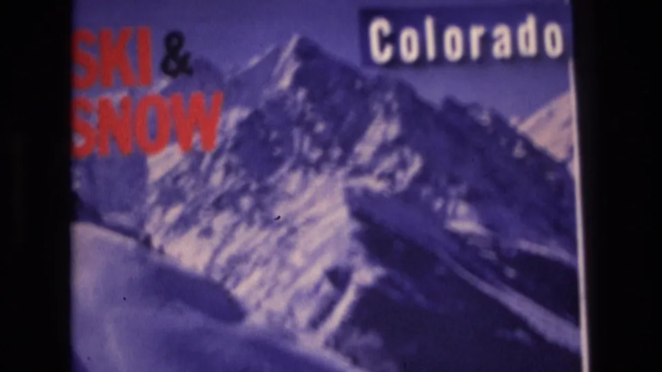 1974 Vail, Colorado home-movie still showing a cropped travel poster with bold red ski text, white Colorado lettering, and a soft purple mountain landscape.
