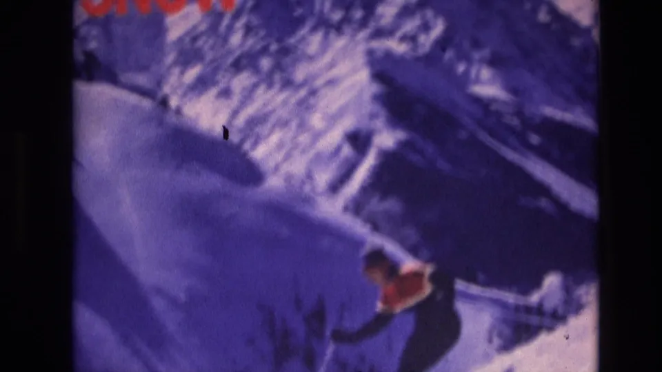 The 1974 Vail home-movie frame shows a skier crossing a snow-covered slope, with ski tracks, deep blue shadows, and visible 8mm grain.