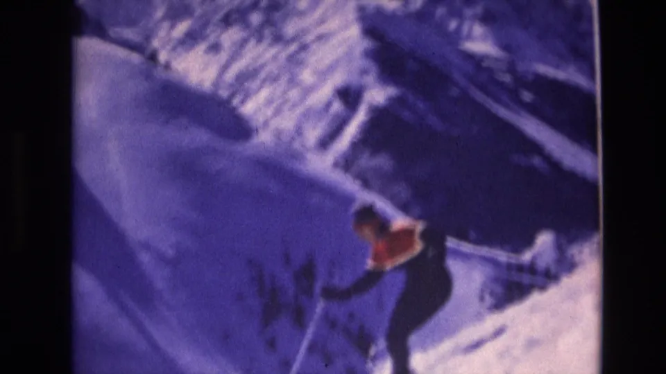 A skier continues downhill on a snowy Vail, Colorado slope in the supplied 1974 8mm footage, framed by purple-blue snow shadows and soft home-movie focus.