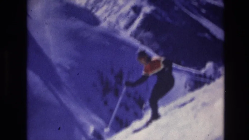 The skier appears mid-descent on the snowy Vail slope, with blue cast, visible grain, and dark film-strip borders emphasizing the home-movie scan.