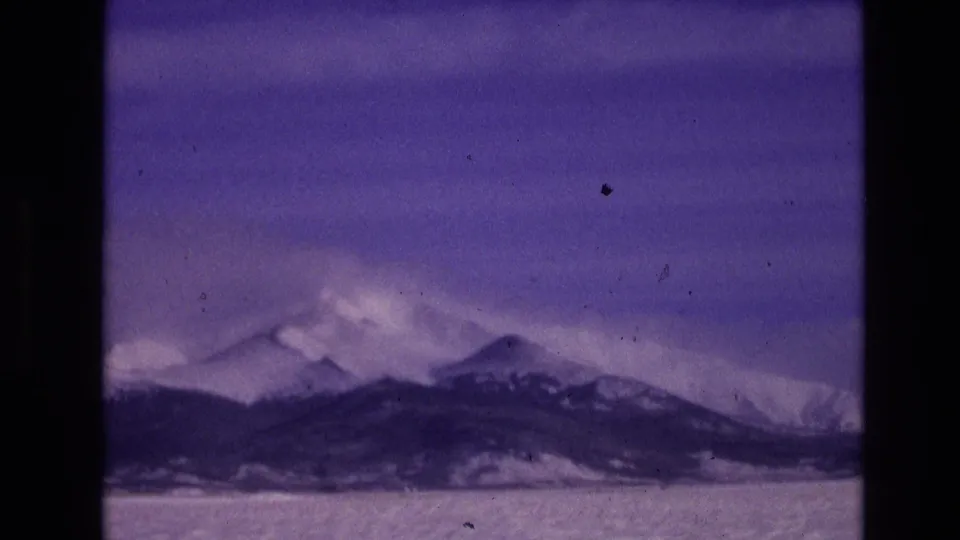 1974 Vail, Colorado 8mm landscape frame showing snow-covered mountain ridges under a cloudy winter sky.