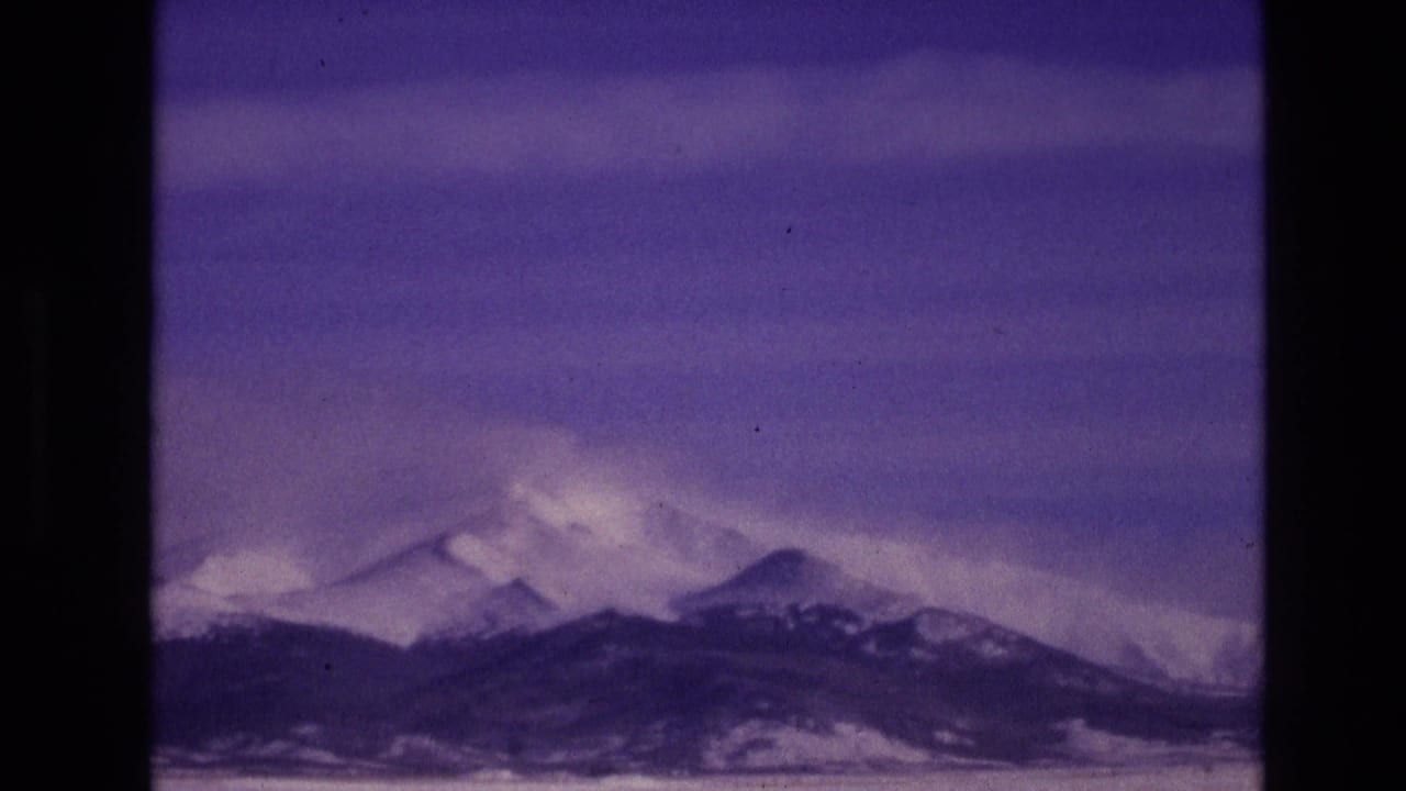 1974 8mm home-movie frame from Vail, Colorado showing distant snow-covered mountain peaks under a purple-blue sky with visible film grain and gate edges.