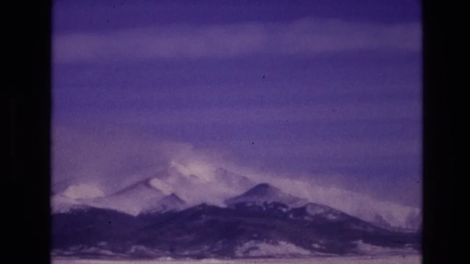 1974 8mm home-movie frame from Vail, Colorado showing distant snow-covered mountain peaks under a purple-blue sky with visible film grain and gate edges.