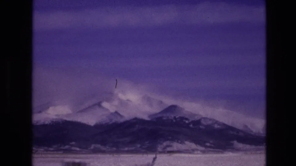 1974 Vail, Colorado 8mm frame showing a snowy Rocky Mountain ridge under a purple sky, with grain, dust, and scratches visible from the original film scan.