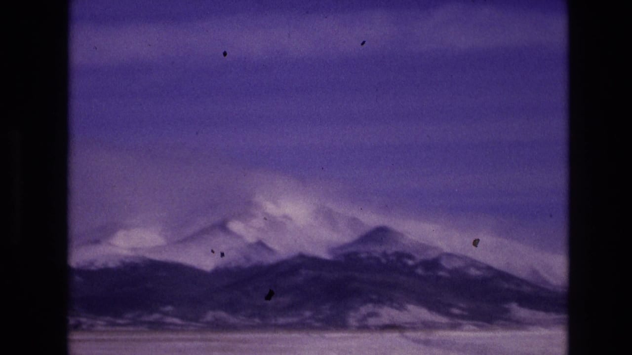 1974 Vail, Colorado 8mm frame showing a distant snow-topped mountain skyline under a purple-blue sky with visible grain, dust, and dark film borders.