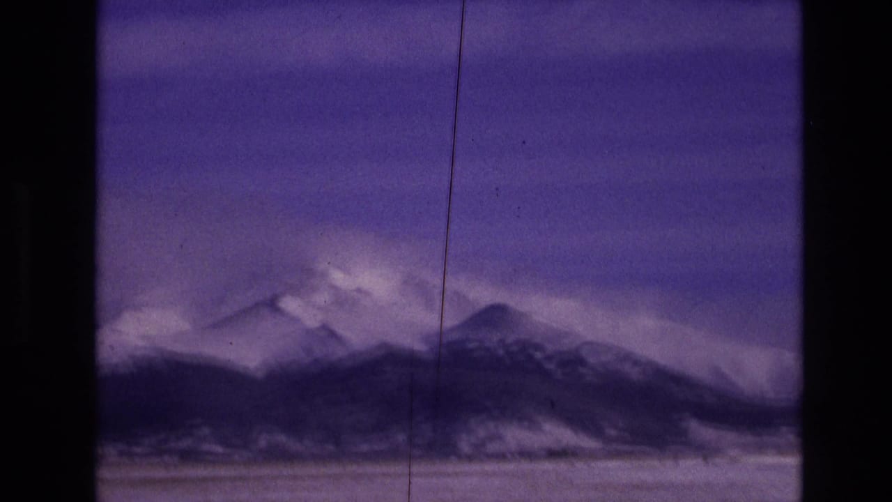 Distant snow-covered peaks and dark ridgeline framed by scratches and film borders.