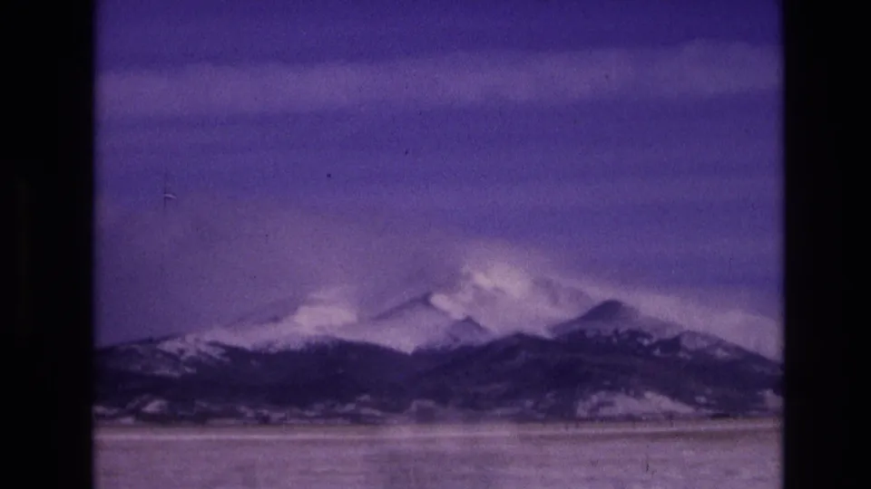 1974 Vail, Colorado 8mm frame of a snow-bright mountain skyline and darker lower ridge beneath a purple sky, with scratches, dust, and slight home-movie blur.