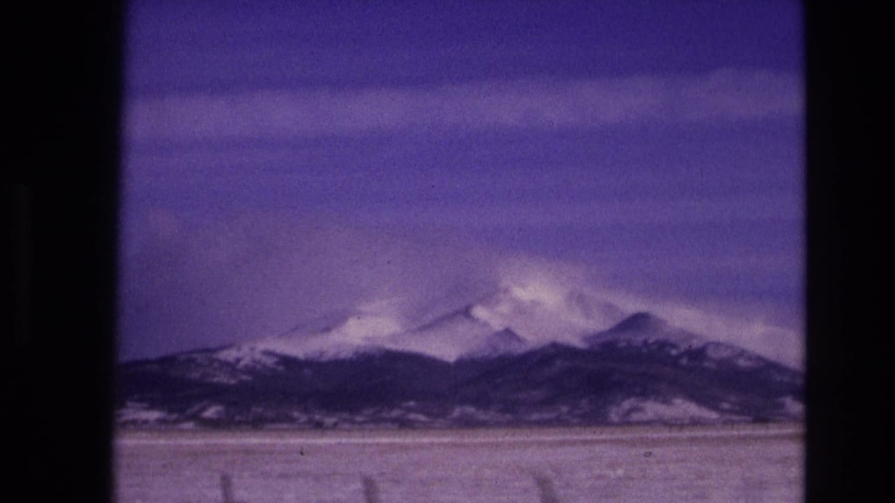 1974 8mm home-movie frame from near Vail, Colorado, showing snow-covered mountains across an open winter plain with purple color shift from the film scan.