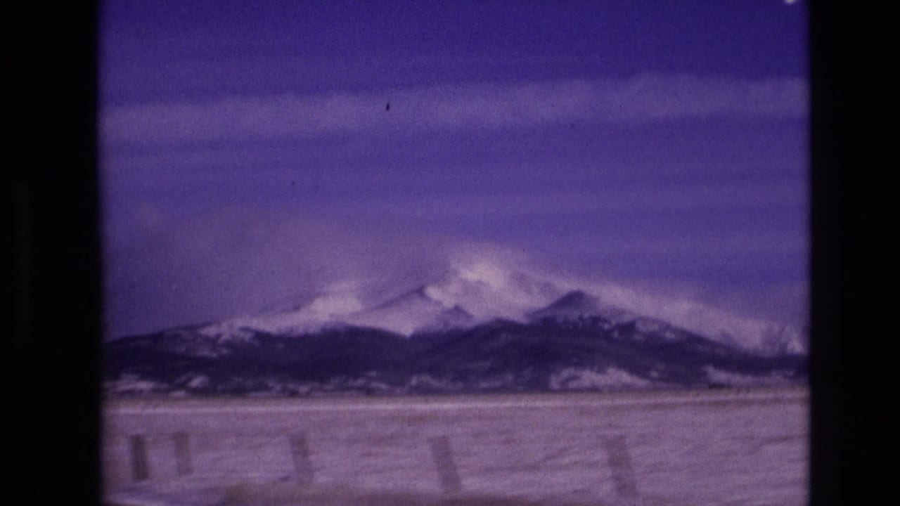 Snowy mountain ridges near Vail, Colorado, appear beyond a broad winter foreground, with visible 8mm frame borders and a strong purple color cast.