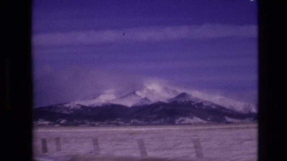Snowy mountain ridges near Vail, Colorado, appear beyond a broad winter foreground, with visible 8mm frame borders and a strong purple color cast.