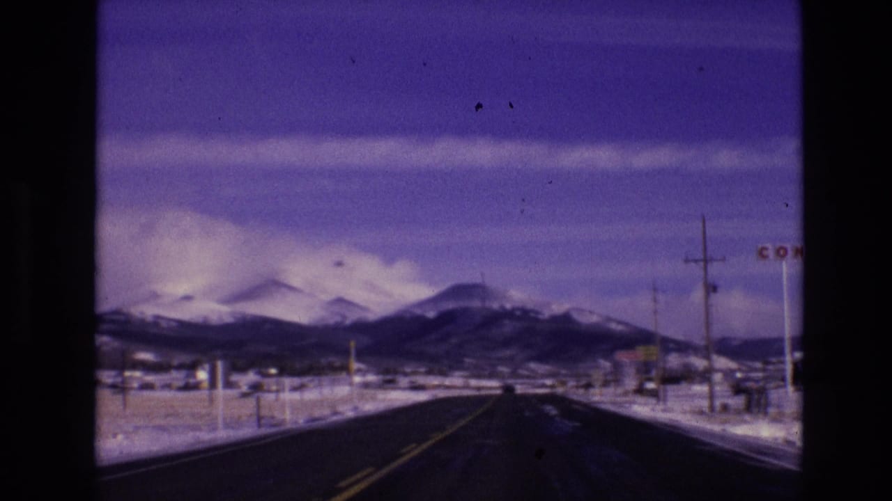 1974 8mm home-movie frame from Vail, Colorado, showing a dark road, snow-covered roadside, utility poles, and a distant mountain range.