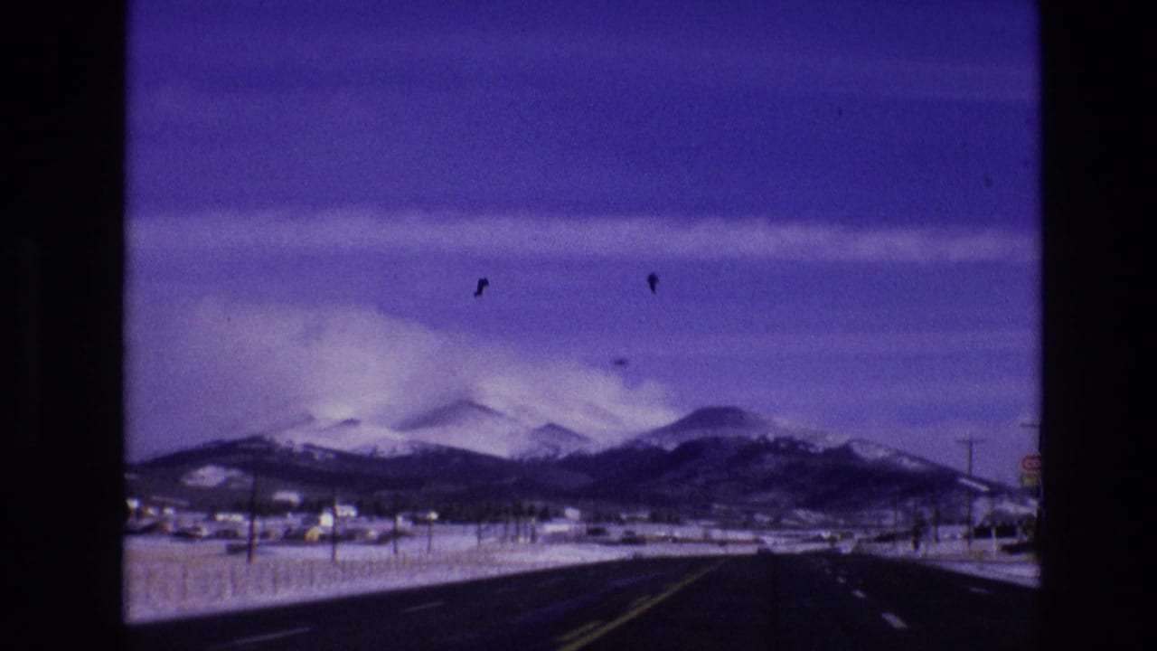 1974 Vail, Colorado 8mm frame showing a dark road leading toward snow-covered mountains under a purple-blue sky.