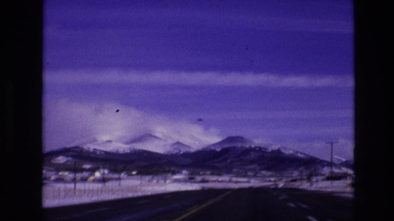 1974 Vail, Colorado home-movie frame with a winter road, utility poles, scattered buildings, and snow-covered mountain slopes.
