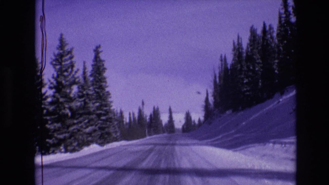 1974 Vail, Colorado frame of a plowed winter road curving through snowbanks and dark evergreen forest.