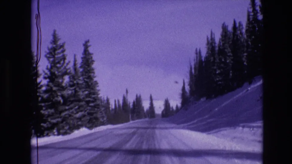 1974 Vail, Colorado frame of a plowed winter road curving through snowbanks and dark evergreen forest.