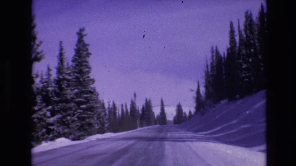 1974 Vail, Colorado home-movie view looking forward along a snowy mountain road lined with evergreens and roadside snowbanks.