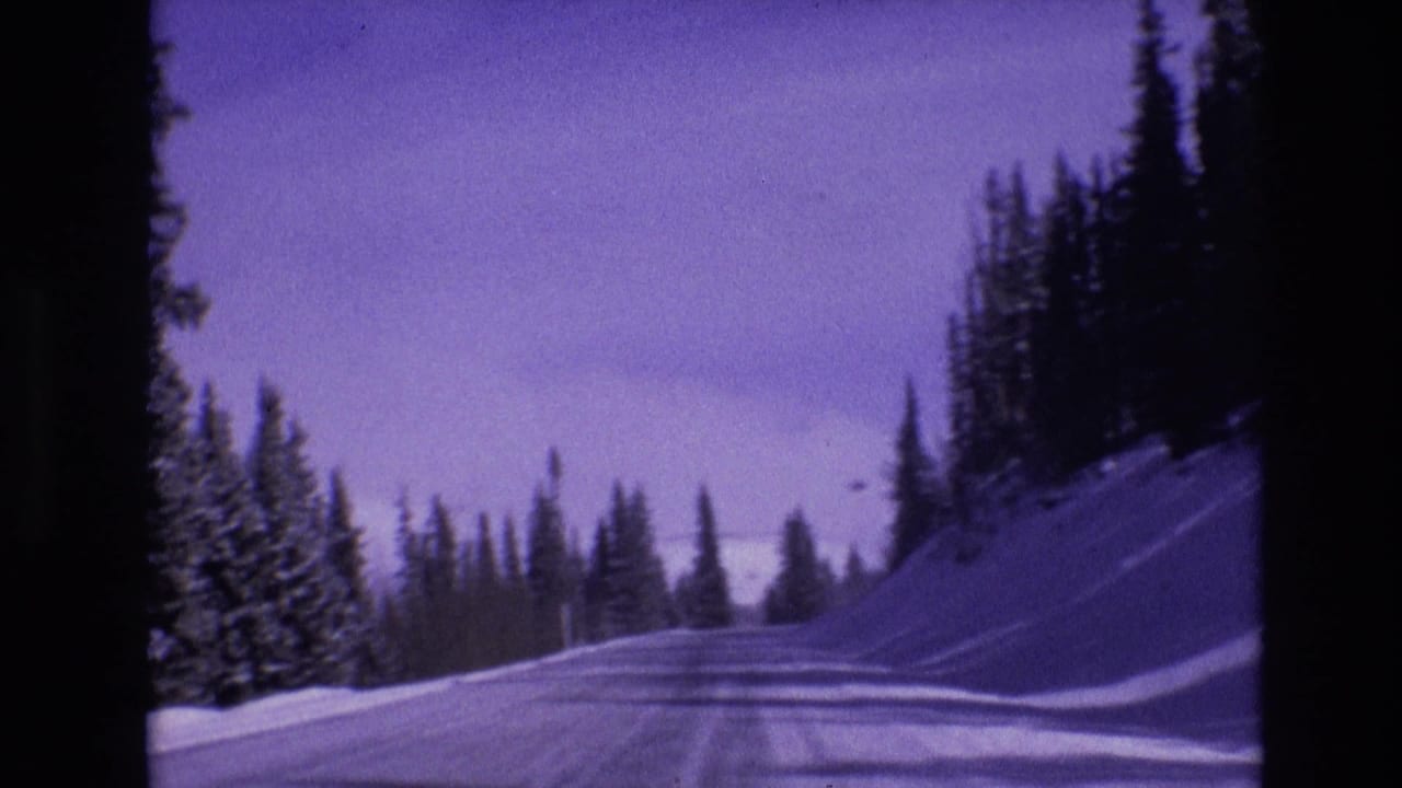1974 Vail, Colorado 8mm frame showing a snowy road curving through evergreen trees with tire tracks, snowbanks, and a purple film cast.