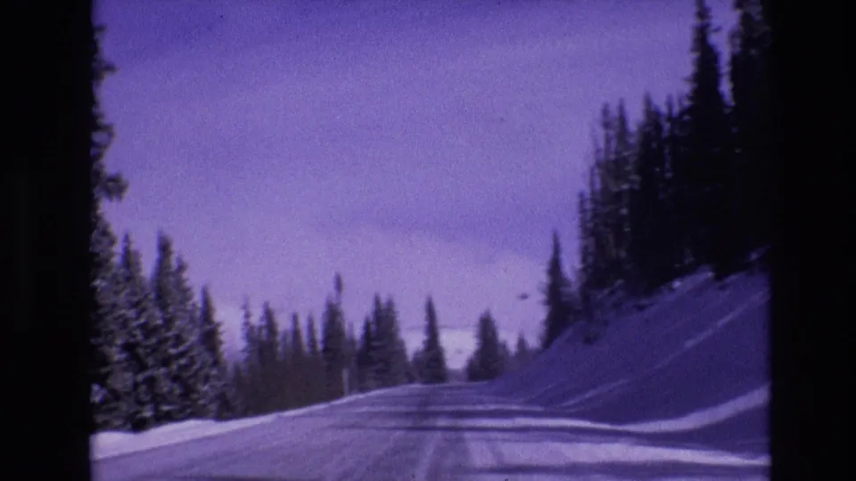 1974 Vail, Colorado 8mm frame showing a snowy road curving through evergreen trees with tire tracks, snowbanks, and a purple film cast.