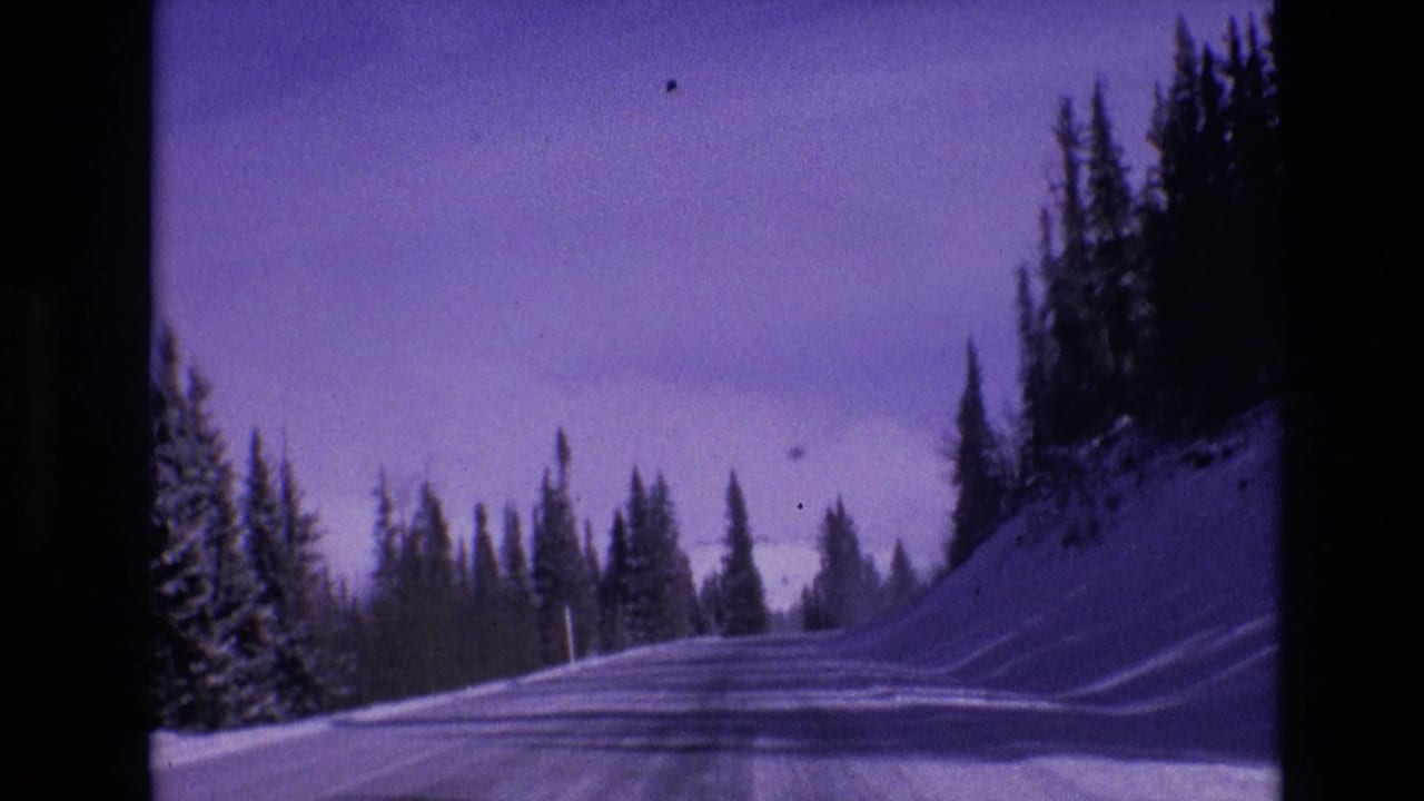 1974 Vail, Colorado 8mm frame with a forward-facing view along an icy snow-covered mountain road lined by evergreens and high snowbanks.