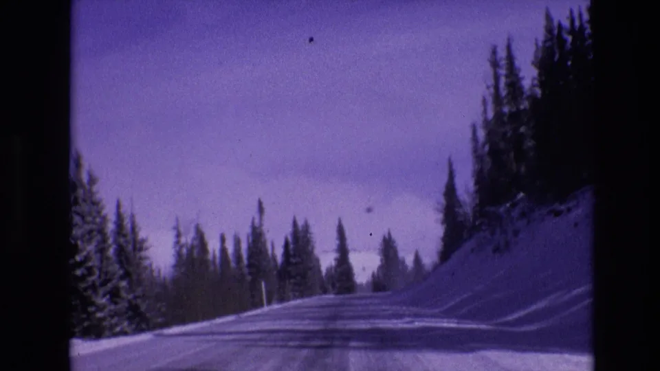 1974 Vail, Colorado 8mm frame with a forward-facing view along an icy snow-covered mountain road lined by evergreens and high snowbanks.