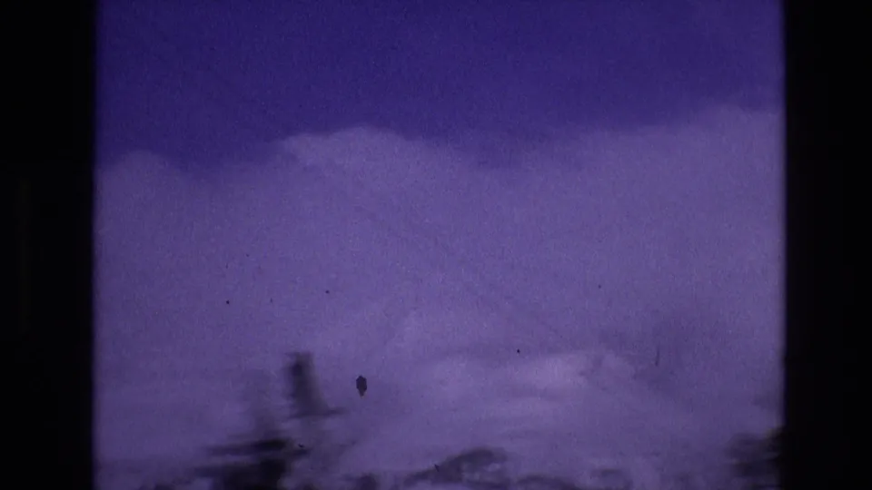1974 Vail, Colorado home-movie frame with distant snow-covered mountain shapes, blurred evergreen silhouettes, and pronounced blue-purple film color shift.