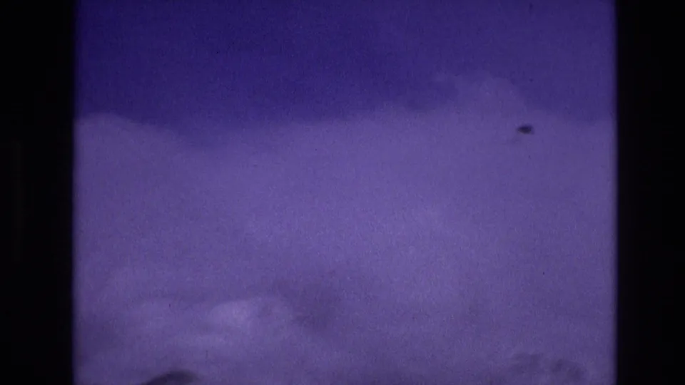 Vail, Colorado 1974 8mm frame showing a soft, snow-covered foreground with dark evergreen silhouettes and visible film grain during a mountain drive.
