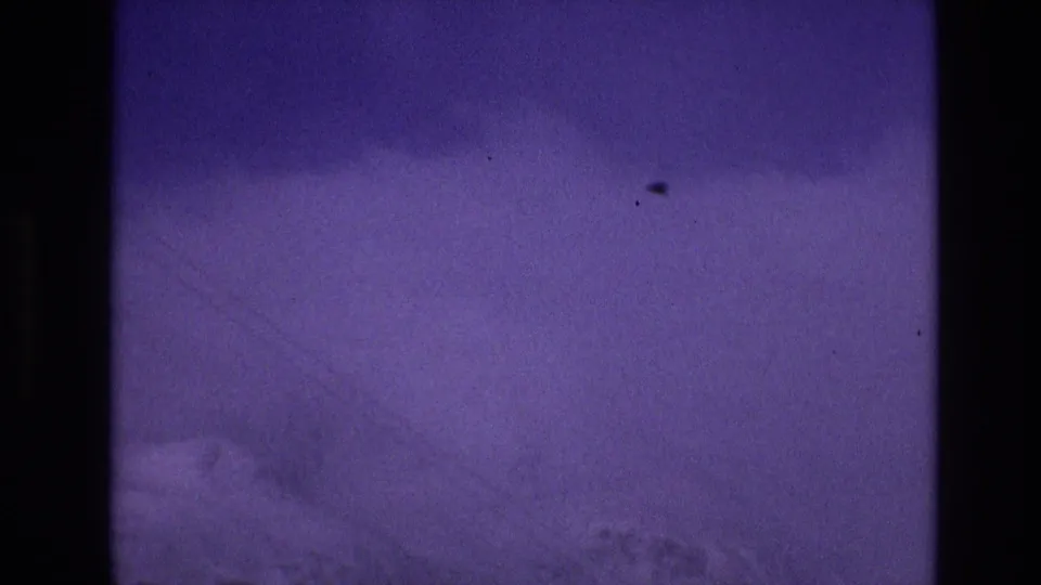 1974 8mm Vail, Colorado frame showing a snowy open slope or roadside clearing with faint tracks, distant evergreen shapes, and strong blue-purple color shift.