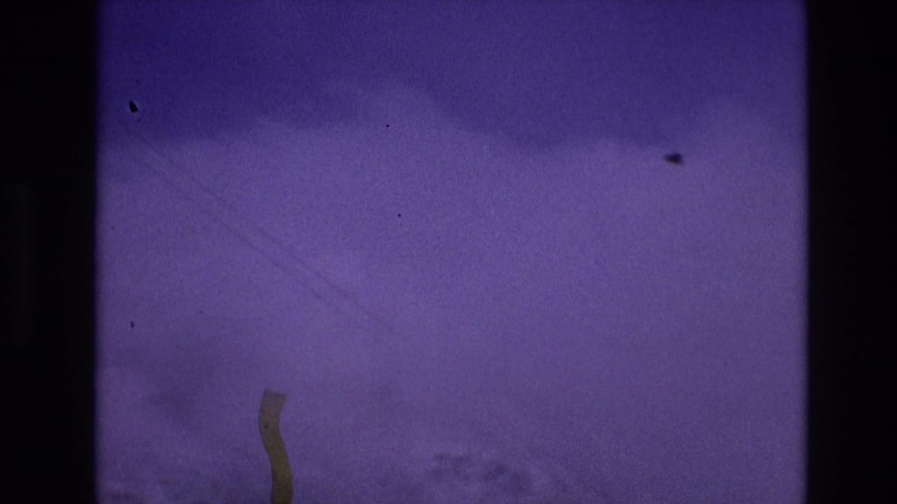 1974 Vail, Colorado 8mm frame showing a distant snow-covered slope under a purple-shifted sky, bordered by dark film gate edges and visible dust.