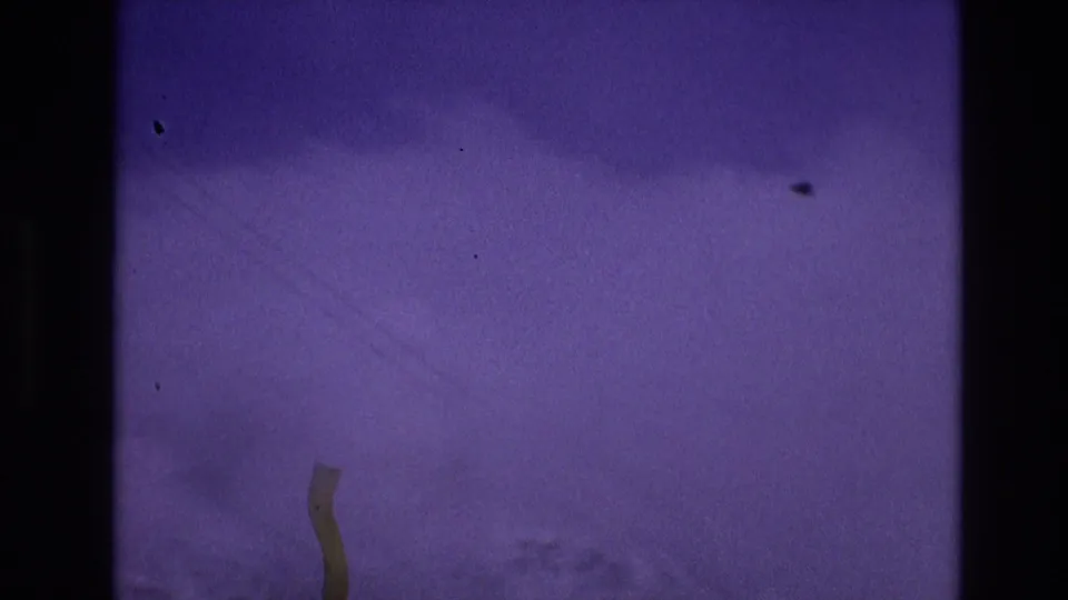 1974 Vail, Colorado 8mm frame showing a distant snow-covered slope under a purple-shifted sky, bordered by dark film gate edges and visible dust.