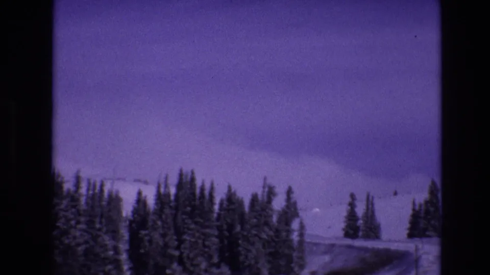 1974 Vail, Colorado 8mm frame showing snow-covered evergreens and a winding road or cleared route through a winter mountain landscape.
