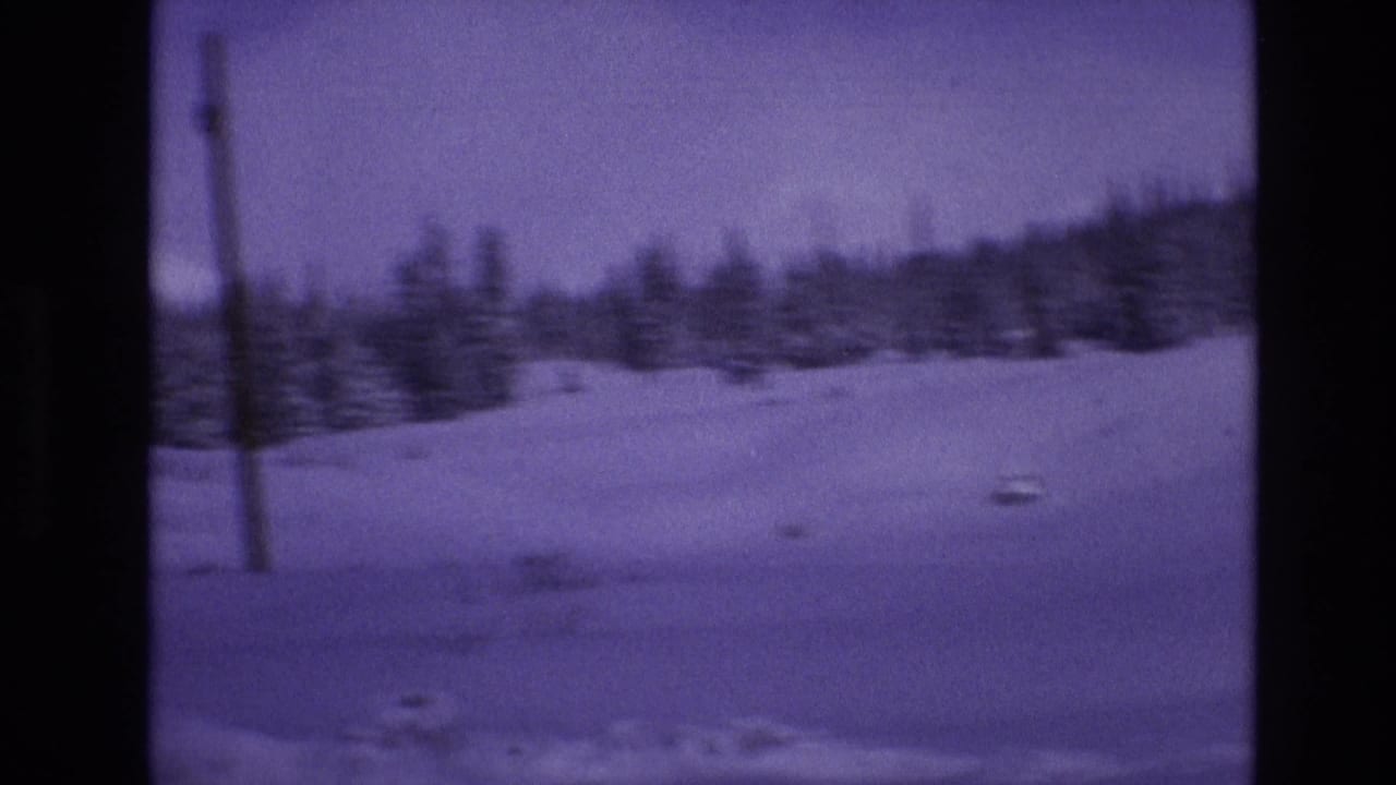 1974 Vail, Colorado frame from moving 8mm footage showing a snowfield, evergreen trees, and a wooden utility pole in a purple-tinted winter view.