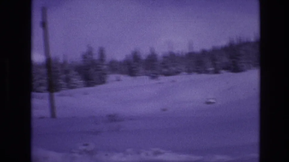 1974 Vail, Colorado frame from moving 8mm footage showing a snowfield, evergreen trees, and a wooden utility pole in a purple-tinted winter view.