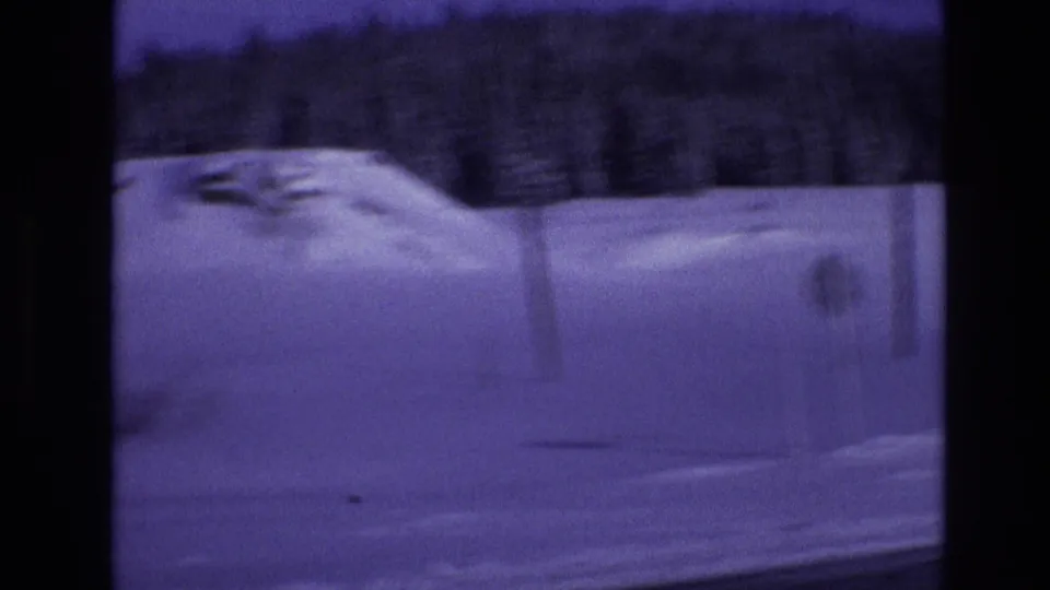 1974 Vail, Colorado home-movie frame showing a snowbank and dark evergreen tree line, softened by motion blur and the aged purple film cast.