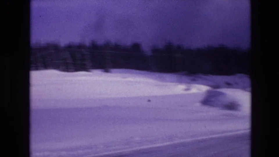 1974 Vail, Colorado 8mm frame showing a broad snowy slope or roadside bank with a distant dark tree line beneath a purple-tinted sky.