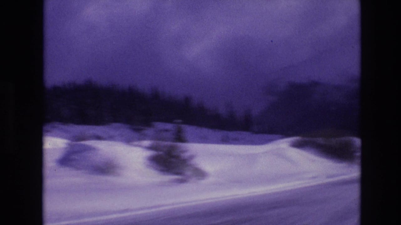 1974 Vail, Colorado 8mm frame showing a snowy roadside foreground, dark evergreen tree line, and purple-blue winter sky seen from a moving vehicle.