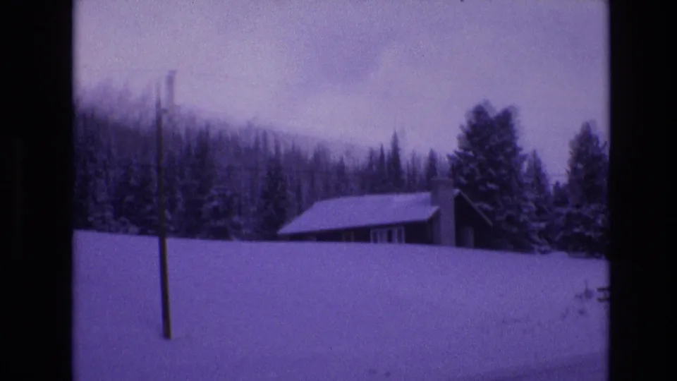 1974 Vail, Colorado frame of a snow-covered cabin or outbuilding set below evergreen trees, with a utility pole and overhead wire visible.