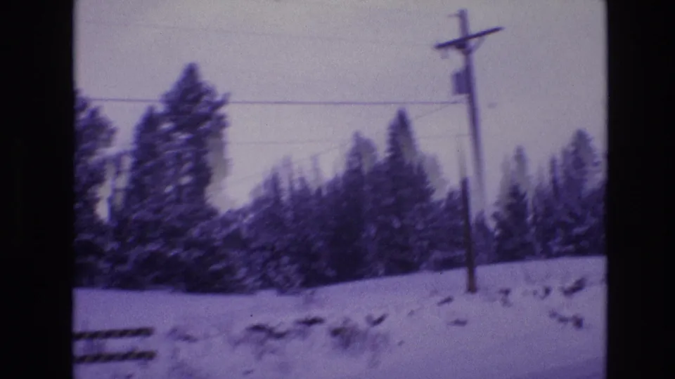 1974 Vail, Colorado frame with a utility pole, overhead line, snow-covered evergreens, low fence sections, and a snowy roadside or field edge.