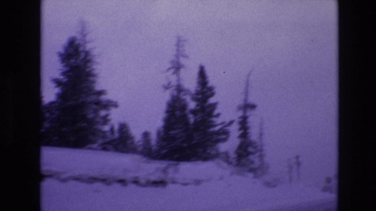 1974 Vail, Colorado winter travel frame showing snow piled along the roadside, dark evergreens, and a utility pole under soft purple-tinted light.