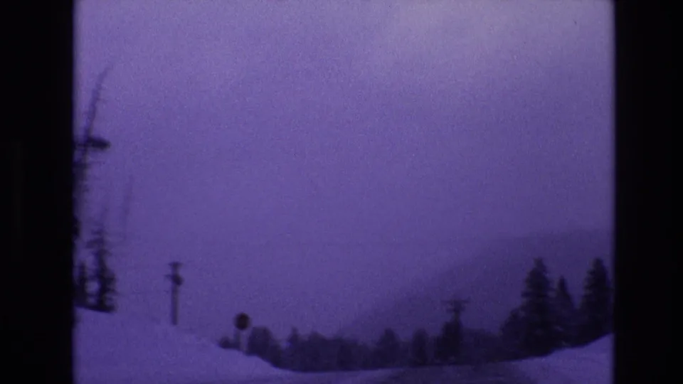 1974 8mm frame near Vail, Colorado showing a snowy country road scene with utility poles, roadside trees, and a hazy mountain backdrop.