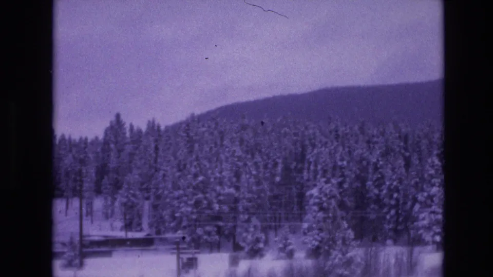 Vail, Colorado winter landscape in 1974 metadata, with snowy evergreens, a low mountain slope, and dark frame edges from 8mm home-movie film.