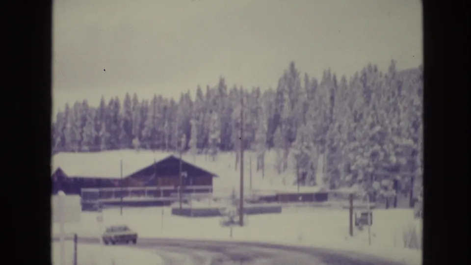 A 1970s-era car travels or sits on a snowy road near a rustic wooden building in the supplied Vail, Colorado winter footage.