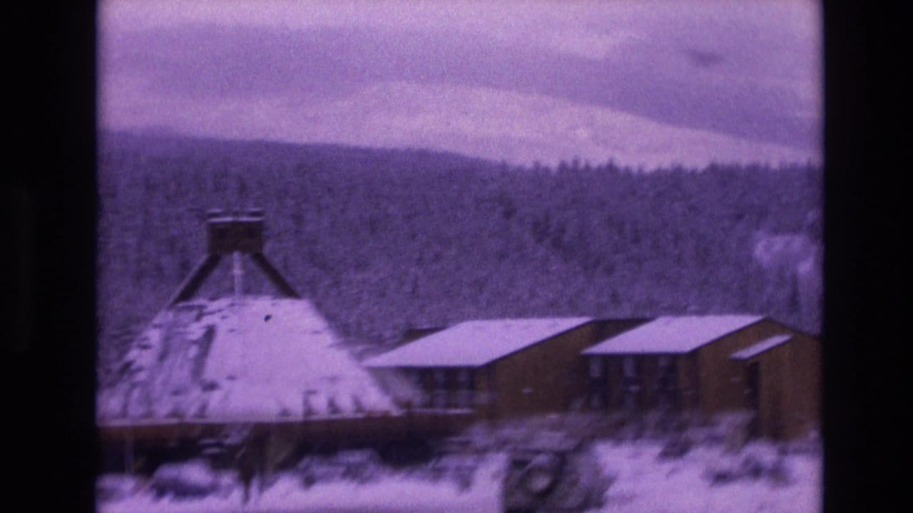 1974 Vail, Colorado 8mm frame showing a snow-covered conical-roof building near low wood structures under an overcast mountain sky.