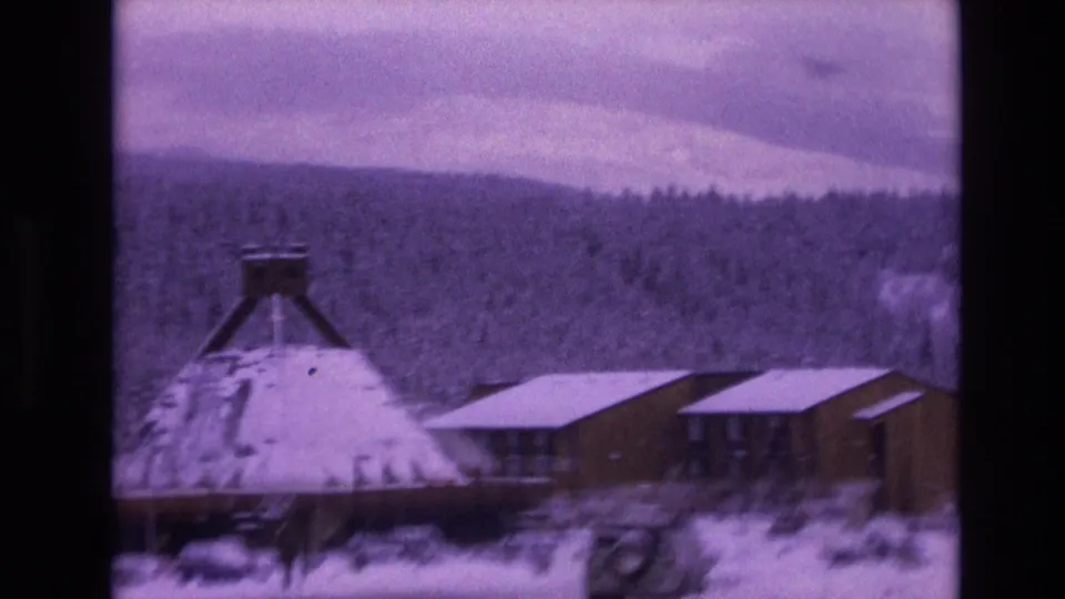 1974 Vail, Colorado 8mm frame showing a snow-covered conical-roof building near low wood structures under an overcast mountain sky.