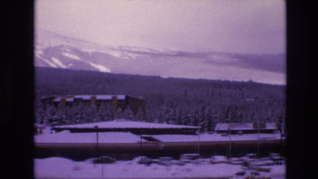 Snowy resort complex with forested hillside and mountain ridge behind it.