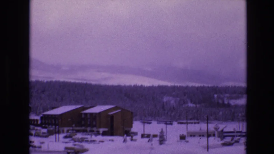 A 1974 Vail, Colorado winter view shows snow-covered resort buildings, parked cars, utility poles, and forested mountain slopes under a purple-blue 8mm color cast.